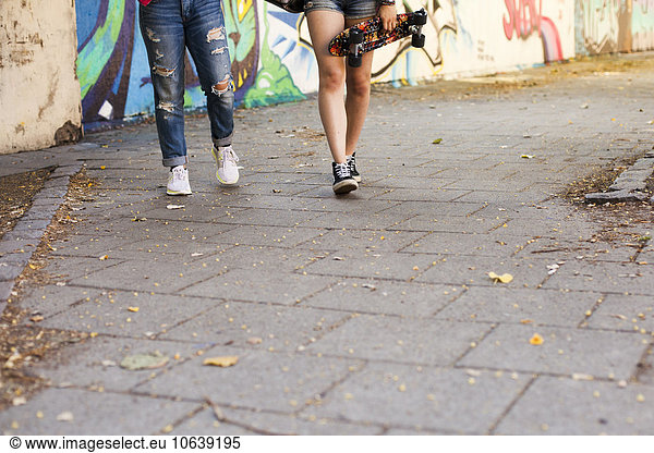 Low section of girls holding skateboards walking on footpath