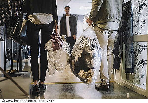 Low section of male and female fashion designers holding plastic bag of recycled clothes at workshop