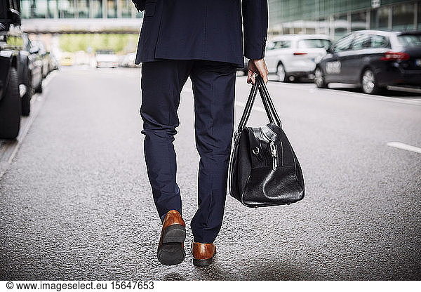 Low section of male lawyer carrying bag while walking on street