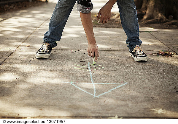 Low section of man drawing arrow symbol on footpath