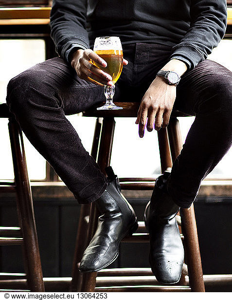 Low section of man holding wineglass while sitting on stool in bar
