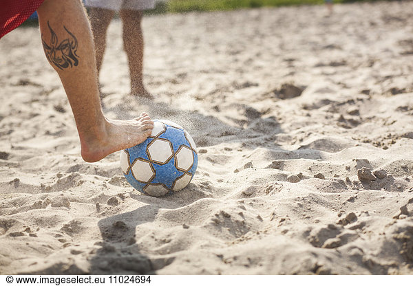 Low section of man playing soccer at beach