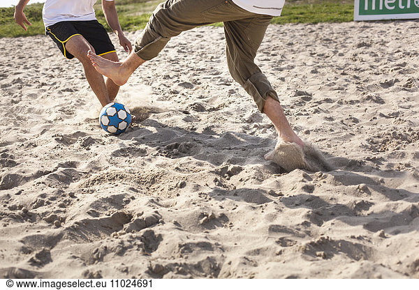 Low section of men playing soccer at beach
