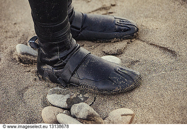 Low section of person wearing wet shoes and standing on sand