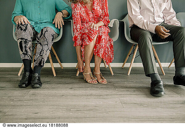 Low section of senior woman adjusting sandal while sitting amidst friends on chairs in dance class