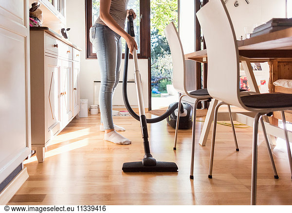 Low section of teenage girl cleaning hardwood floor with vacuum cleaner at home