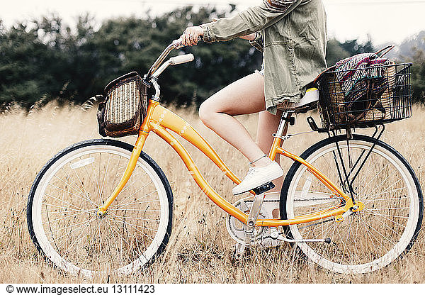 Low section of teenage girl riding bicycle amidst grassy field