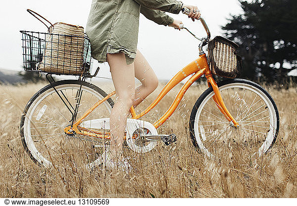 Low section of teenage girl riding bicycle amidst plants on field