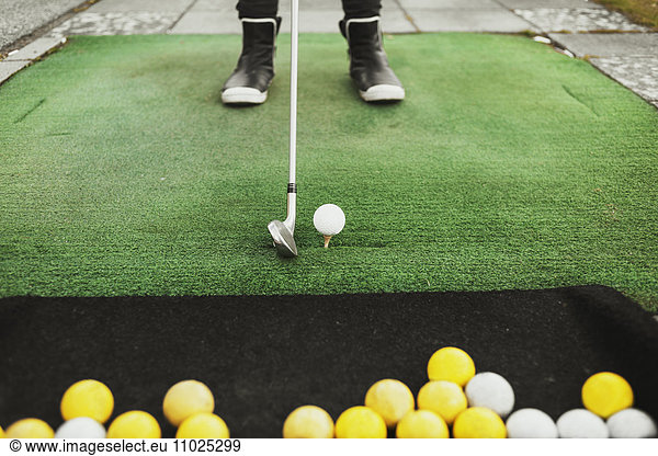 Low section of woman aiming golf ball at driving range