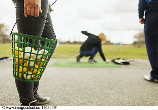 Low section of woman holding basket with balls at golf course