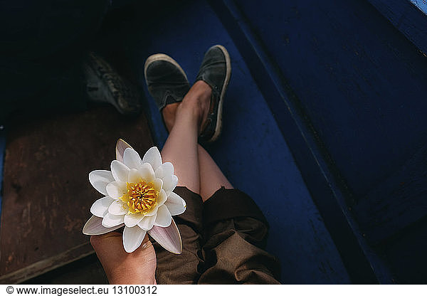 Low section of woman holding lotus water lily while sitting in boat