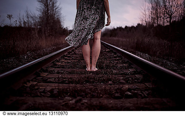Low section of woman standing at railroad tracks against cloudy sky during sunset