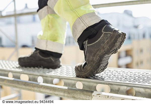Low section of worker walking on metal platform at construction site
