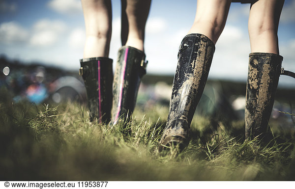 Low section rear view of two young women at a summer music festival wearing muddy Wellington boots.