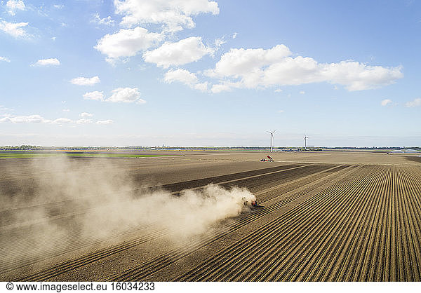 Luftaufnahme eines Traktors  der auf einem von Dürre heimgesuchten Kartoffelfeld in den Niederlanden Staub aufwirbelt.