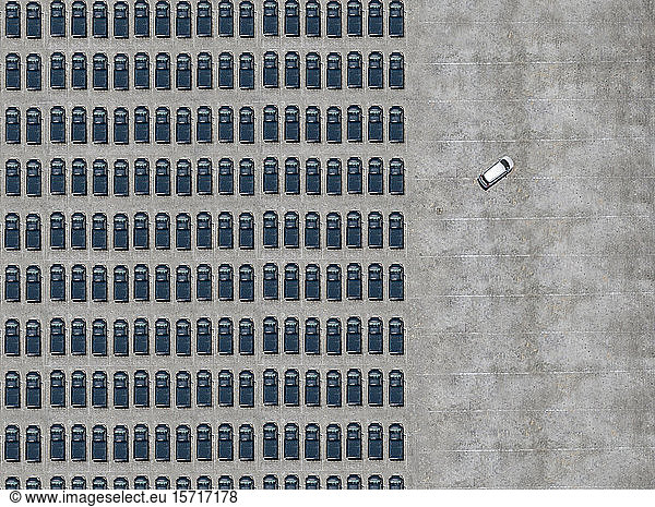 Luftaufnahme eines weißen Autos  das einen mit schwarzen Autos gefüllten Parkplatz verlässt