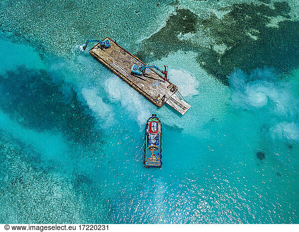 Luftaufnahme von Erdbewegungsmaschinen  die Masten auf einer schwimmenden Plattform im Male-Atoll transportieren