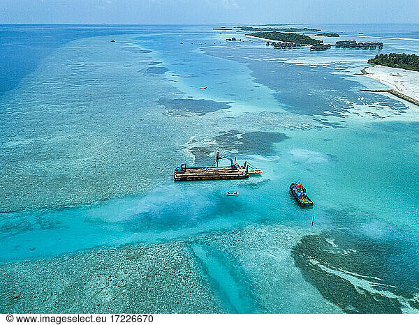 Luftaufnahme von Erdbewegungsmaschinen  die Masten auf einer schwimmenden Plattform im Male-Atoll transportieren
