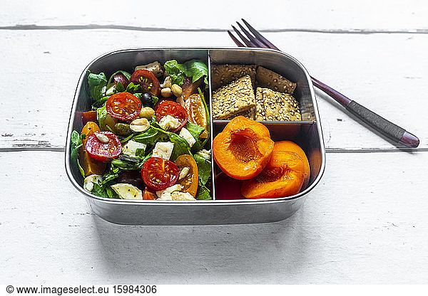 Lunch box with rocket salad with colored tomatoes  mozzarella and nuts  crispbread and apricots  wooden fork