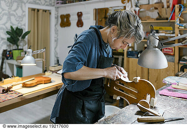 Luthier carving on violin at desk in workshop