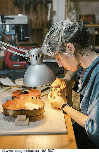 Luthier working on bridge part of violin at desk in workshop