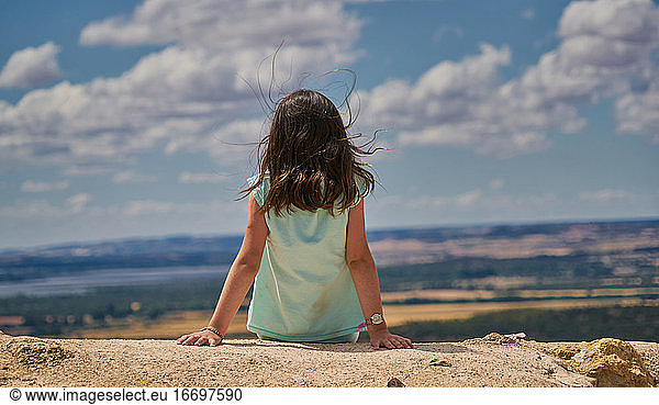 Mädchen auf dem Rücken sitzend in Landschaft und blauem Himmel mit weißen Wolken