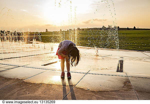 Mädchen beugt sich beim Stehen gegen Springbrunnen im Park