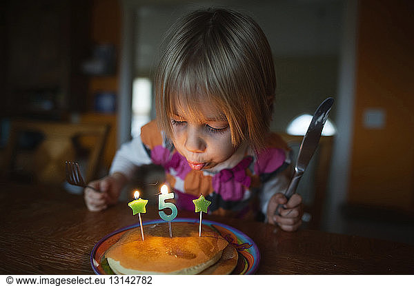 Mädchen bläst Kerzen auf Pfannkuchen