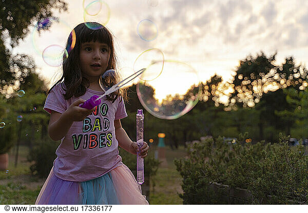 Mädchen  das mit einem Zauberstab Seifenblasen betrachtet  während es bei Sonnenuntergang spielt