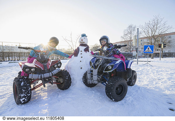 Mädchen fahren Quad und lehnen sich an einen Schneemann