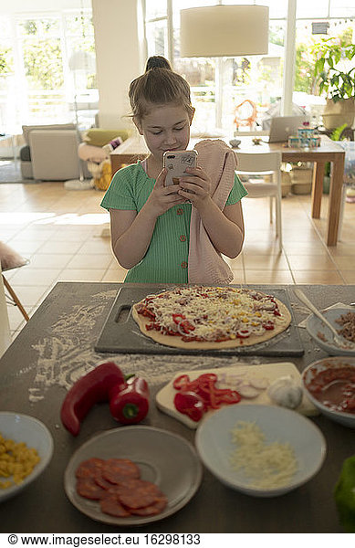 Mädchen fotografiert Pizza über Kücheninsel