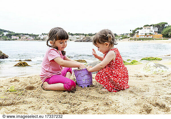 Mädchen geben Sand in einen Eimer am Strand