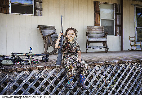 Mädchen hält Gewehr  während sie auf der Veranda sitzt