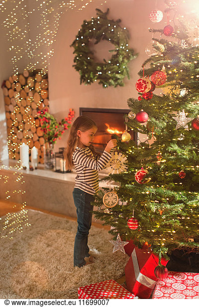 Mädchen hängt Schneeflocke Ornament auf Weihnachtsbaum im Wohnzimmer