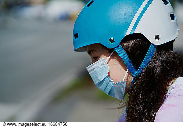 Mädchen in Maske und Helm fahren Kick-Scooter auf der Straße in der Stadt Straße