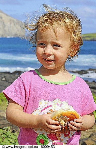 Mädchen isst einen Keks am Strand von Makapu'u am östlichen Ende der Insel. Ansichten  mit Manana Island. O'ahu. Hawaii.