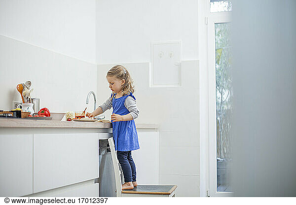 Mädchen isst Essen  während sie auf einem Stuhl in der Küche zu Hause steht