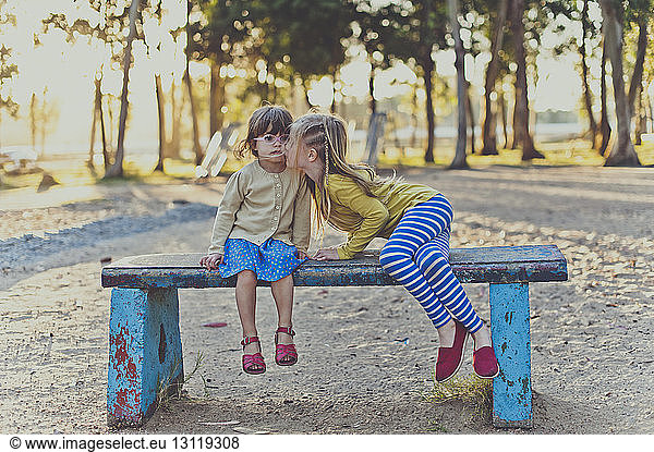 Mädchen küsst Schwester auf Parkbank sitzend
