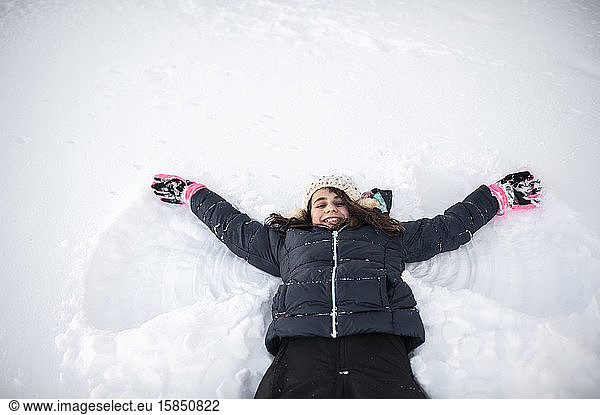Mädchen lächelt beim Schnee-Engel machen im Schnee im Vorgarten