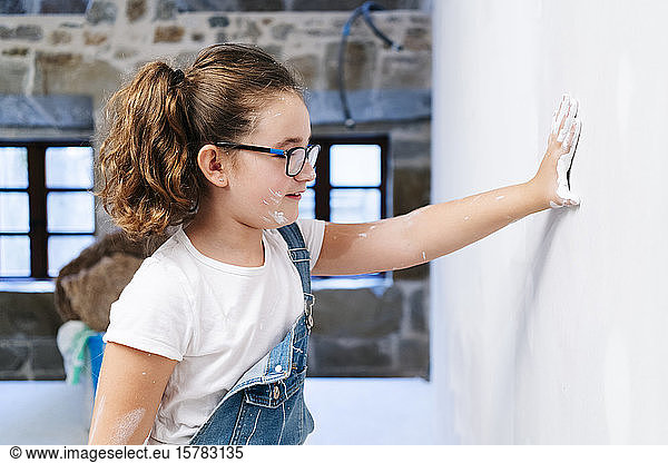 Mädchen mit Farbe auf der Hand  das eine Wand in einem Haus berührt