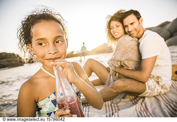 Mädchen mit ihrer Familie bei Sonnenuntergang am Strand bei einem Erfrischungsgetränk