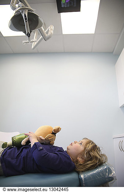 Mädchen mit Spielzeug  das auf einem Krankenhausbett liegt und auf Geräte in der Decke schaut