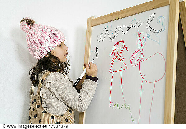 Mädchen mit Strickmütze  die zu Hause am Whiteboard zeichnet