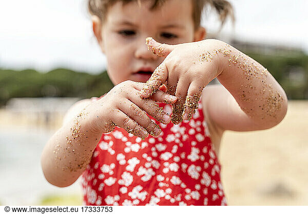 Mädchen schaut auf schmutzige Hände  während sie am Strand steht