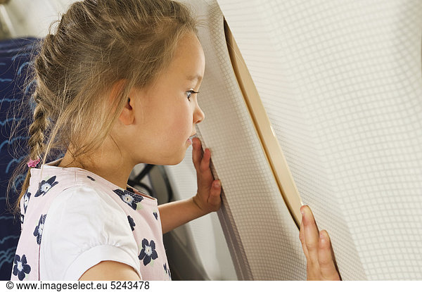 Mädchen schaut durchs Fenster im Economy Class Flugzeug