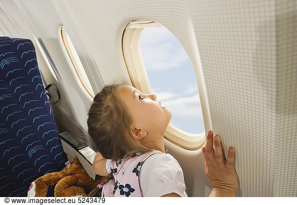 Mädchen schaut durchs Fenster im Economy Class Flugzeug