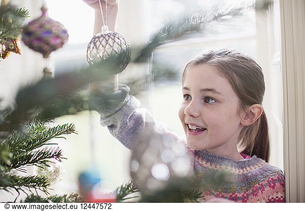 Mädchen schmückt  hängt Ornament an Weihnachtsbaum