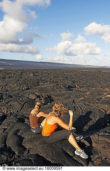 Mädchen sitzen über den schwarzen Lavabergen in der Nähe der Küste und des Highways Chain of Crater Road. Hawai'i Volcanoes National Park. Big Island. Hawaii. Lavafelder und der Pazifische Ozean mit einem Fischaugenobjektiv  Volcano National Park. Jüngster Lavastrom  Lava vom Typ Pahoehoe. Der 1916 gegründete Hawai?i Volcanoes National Park ist ein Nationalpark der Vereinigten Staaten und liegt im US-Bundesstaat Hawaii auf der Insel Hawaii. Er umfasst zwei aktive Vulkane: Kilauea  einer der aktivsten Vulkane der Welt  und Mauna Loa  der mächtigste subaerische Vulkan der Welt. Der Park bietet Wissenschaftlern Einblicke in die Entstehung der Hawaii-Inseln und in laufende Studien über die Prozesse des Vulkanismus. Für Besucher bietet der Park dramatische Vulkanlandschaften sowie Einblicke in eine seltene Flora und Fauna. In Anerkennung seiner herausragenden Naturwerte wurde der Hawai?i Volcanoes National Park 1980 zum internationalen Biosphärenreservat und 1987 zum Weltnaturerbe ernannt. Im Jahr 2000 wurde empfohlen  den Namen durch den Hawaiian National Park Language Correction Act of 2000 zu ändern und die hawaiianische Schreibweise beizubehalten  aber dieser Gesetzentwurf wurde nicht angenommen. Im Jahr 2012 wurde der Hawai'i Volcanoes National Park auf dem 14. Quartal der America the Beautiful Quarters Serie geehrt.