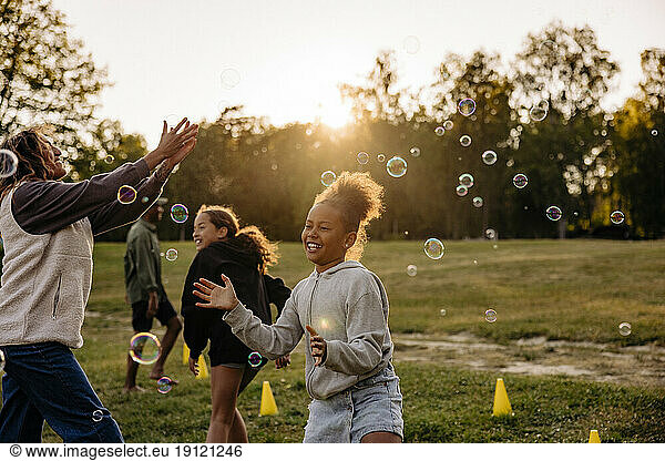 Mädchen spielt inmitten von Seifenblasen mit Freunden auf dem Spielplatz im Ferienlager