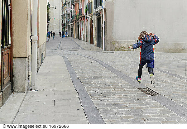 Mädchen springt auf einem Spaziergang in der Mitte einer Straße in der Altstadt